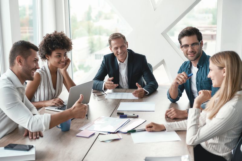 Teamwork. Multicultural team discussing something and smiling while sitting at the office table